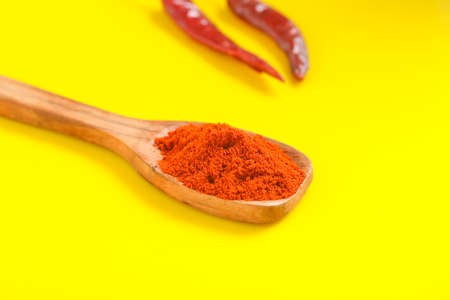 Chilli powder in wooden spoon with dry red chilly on yellow background.の写真素材