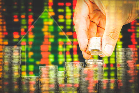 Finance and Saving money banking concept,Hope of investor concept,Male hand putting money coin like stack growing business. double exposure of blur background display of Stock market quotesの写真素材