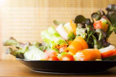 Close up of fresh salad of lettuce, cucumber and tomato on plate for healthy eating.Fresh vegetable salad in Black plate  on wood table. Salad for healthy. Fresh raw vegetables salad background.の写真素材