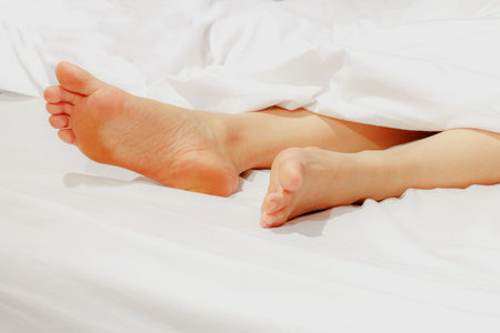 Under the covers with feet showing in a bedの写真素材