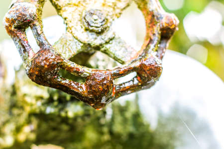 A close up of a rusted valve connects to water supply with metal pipe,Industrial metal water tab,seen in a garden, for watering the plantsの写真素材