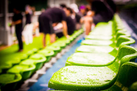 Close up chair green,green plastic stadium seats arranged in a row. The image has been made before the beginning of a tennis game,Blurred background of crowd of people at the stadiumの写真素材