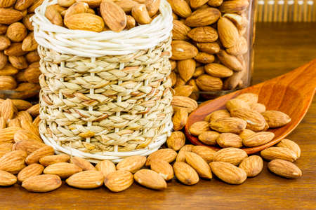 Almonds seeds pour from wood spoon on textured wooden background, top view.の写真素材