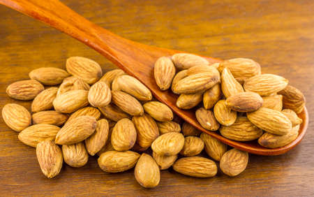 Almonds seeds pour from wood spoon on textured wooden background, top view.の写真素材