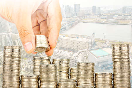 Exposure of Finance and Saving money banking concept,Hope of investor concept,Male hand putting money coin like stack growing business. background the cityの写真素材