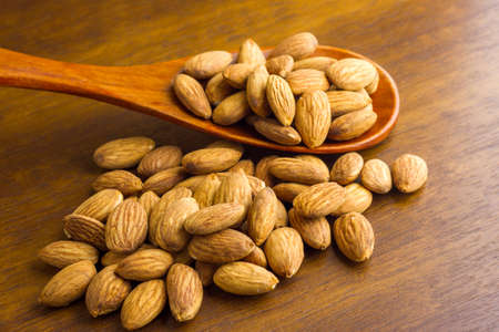 Almonds seeds pour from wood spoon on textured wooden background, top view.の写真素材