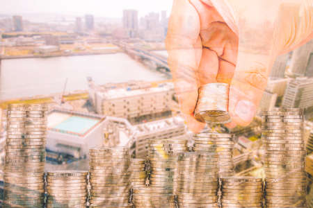 Exposure of Finance and Saving money banking concept,Hope of investor concept,Male hand putting money coin like stack growing business. background the cityの写真素材