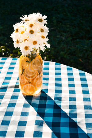 Glass jar decoration filled with lemons and daisies sitting on a picnic table.の写真素材