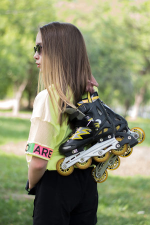 A teenage girl holds roller skates, preparing to roller skate in a park. Concept is to offer...