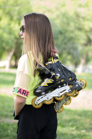 A teenage girl holds roller skates, preparing to roller skate in a park. Concept is to offer...