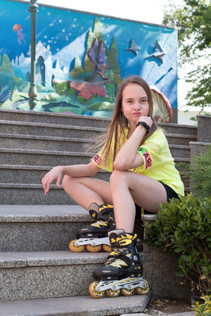 A teenage girl sits in a park wearing roller skates, getting ready to go skating. Concept is to...