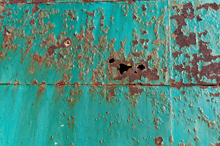 Teal paint on a huge metal door is peeling and rusting