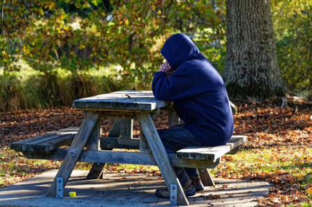 A person with a hood up sits at a picnic table in the parkの写真素材