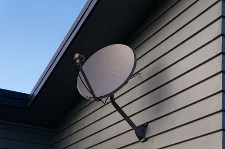 A grey parabolic dish on the side of a weatherboard houseの写真素材