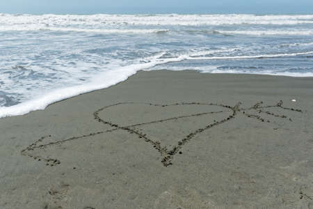 A hand drwan love heart in the sand with an arrow through itの写真素材