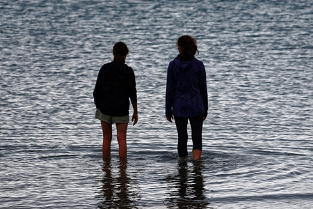 The evening light silhouettes two people taking a paddle in the sea.の写真素材