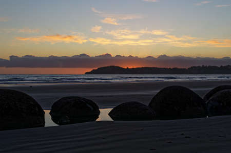 Moeraki Boulders sit in a pool of water on the beach, as the sun comes up, the tide is out.の写真素材