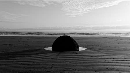 A Moeraki Boulder sits in a pool of water on the beach, the tide is out.の写真素材