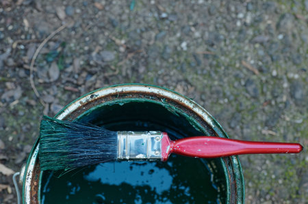 A paint brush waits to be used, it is lying across the top of an open paint can.