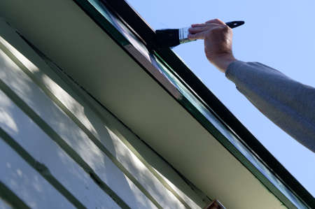 A person holding a paint brush is painting over pink primer that has been painted on a bargeboard in preparation for paintingの写真素材