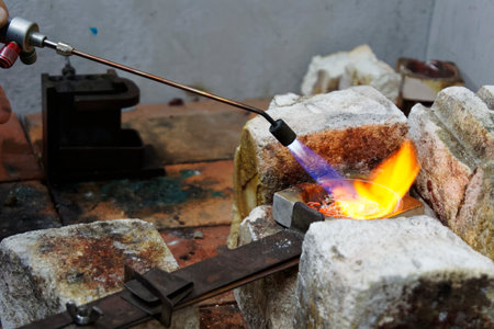 Flames burn brightly as heat is applied to a crucible full of unwanted silver, it is going to be melted down and used for castingの写真素材