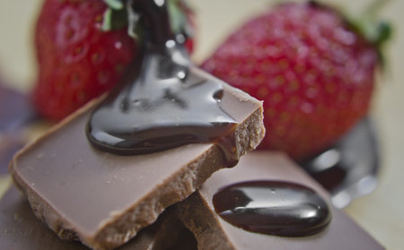 Chocolate syrup poured on chocolate stack. Strawberries in background.