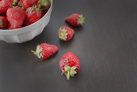 Small white bowl filled with succulent juicy fresh ripe red strawberries on an old wooden textured table top. Selective focus.の写真素材