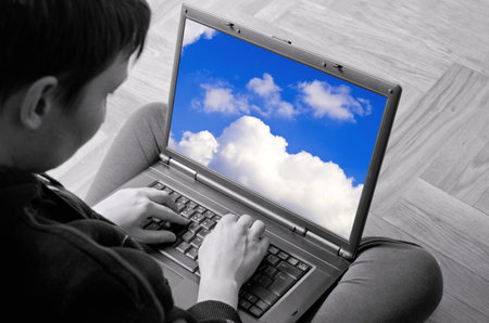 Adult woman typing on laptop. Selective focus on hands and screen with clouds.