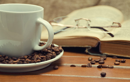 Cup of coffee and old book with reading glasses. Selective focus.の写真素材