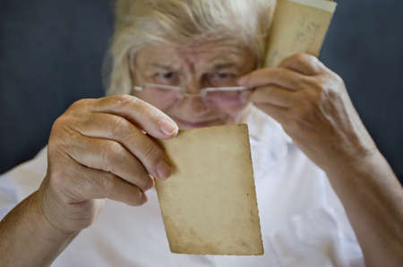 Old photo in hand. An elderly woman watching photo. Remembering the past.の写真素材