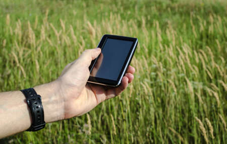 Male hand holds GPS device over grass field. Navigation concept.の写真素材