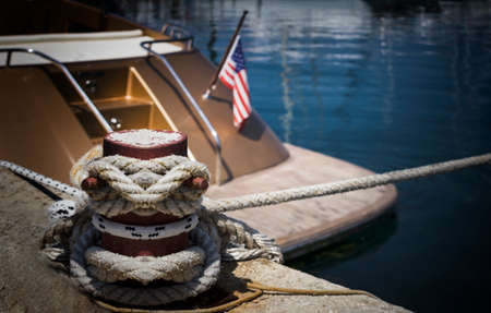 The yacht with the US flag docked at a pier. Selective focus on mooring bollard with nautical rope knotted on it.の写真素材