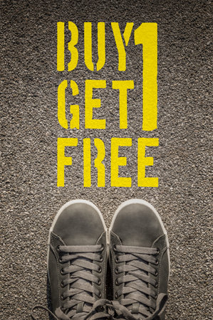 Sneakers with buy one get one free written on the asphalt roadの写真素材