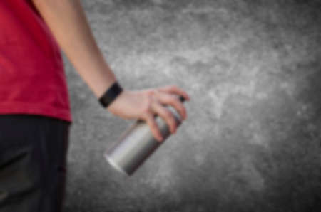 Blurry hand holding a graffiti spray can in front of a dark concrete wallの写真素材