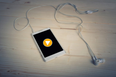 Play button on Smart phone with earphones on wooden table