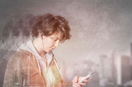 Double exposure of city and woman using earphones from smart phone, listening to music.の写真素材