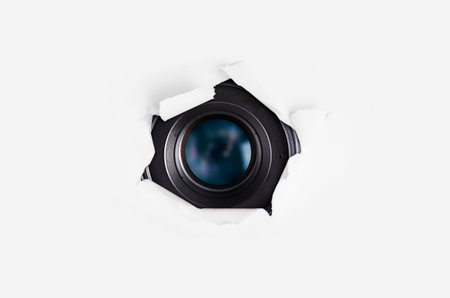 Camera lens hiding behind the paper wall. Spy concept.