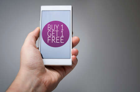 Buy one get one free icon on smart phone in hand on gray backgroundの写真素材