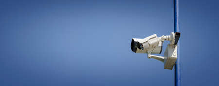 Two surveillance cameras on a pole with blue sky backgroundの写真素材