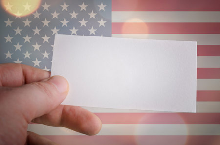 Hand holds a blank business card with the flag of America and bokeh lights in the backgroundの写真素材
