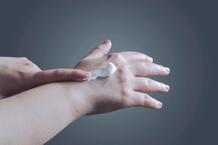 Woman applies cream on her hands isolated on dark backgroundの写真素材