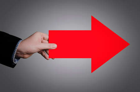 Businessman's hand holding a big red arrow pointing to the rightの写真素材