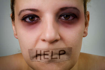 Portrait of woman victim of domestic violence with taped mouth, begging for help.の写真素材