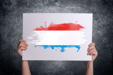 Luxembourg flag on white card in hands. Concept of patriotism, freedom and national pride.の写真素材