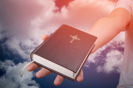 Hand with Holy Bible book and cloud background. Freedom of religion concept.