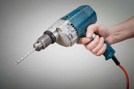 A man's hand with an electric power drill on gray background.の写真素材