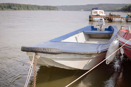 Small boat tied with rope and chain on moody riverの写真素材