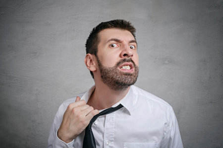 Portrait of rage businessman with beard taking off his tie. Concept of anger. 