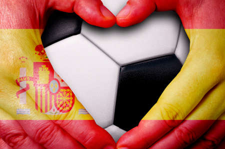 Hands painted with a Spain flag forming a heart over soccer ball backgroundの写真素材