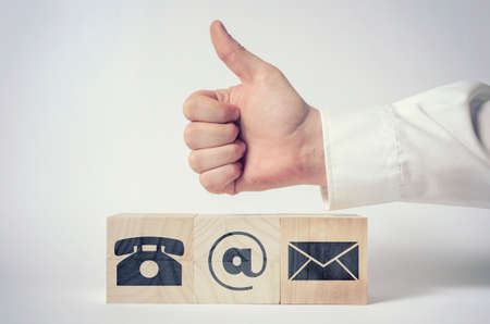 Contact us. Businessman's hand giving thumbs up for communications icons on wooden blocks.の写真素材